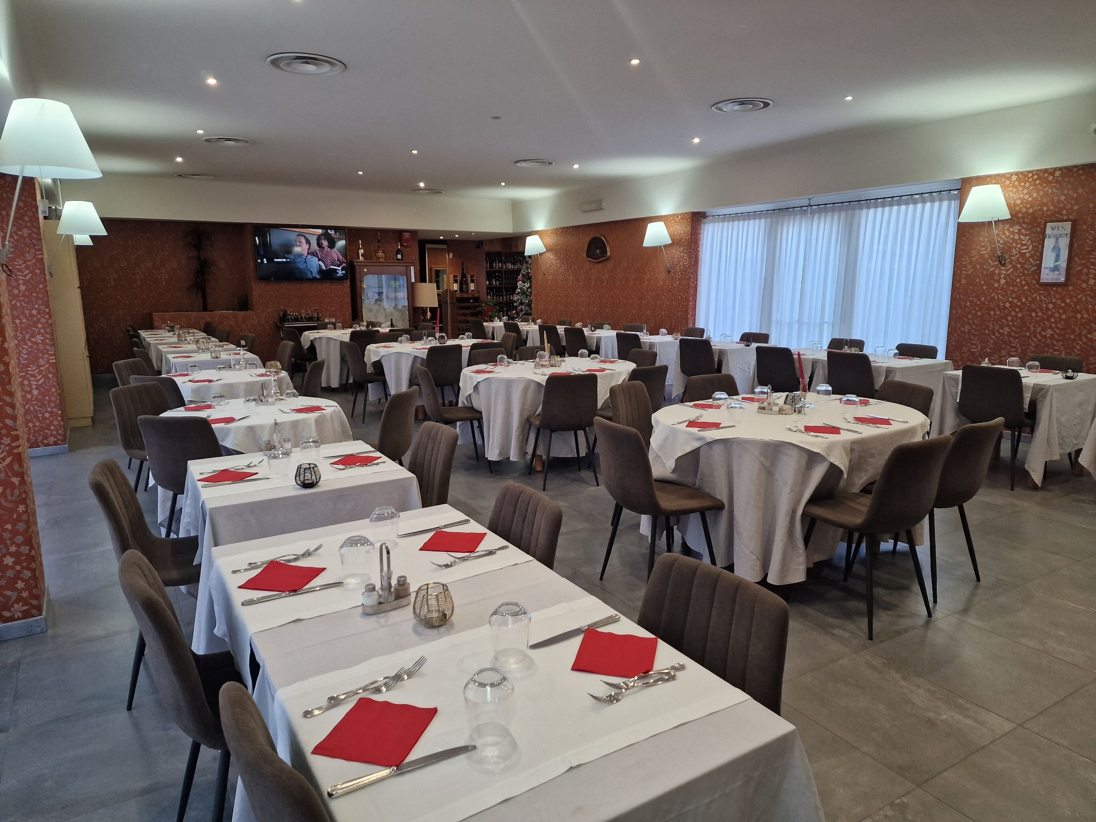 A dining area with round tables set for meals, each with white tablecloths, red napkins, and silverware.
