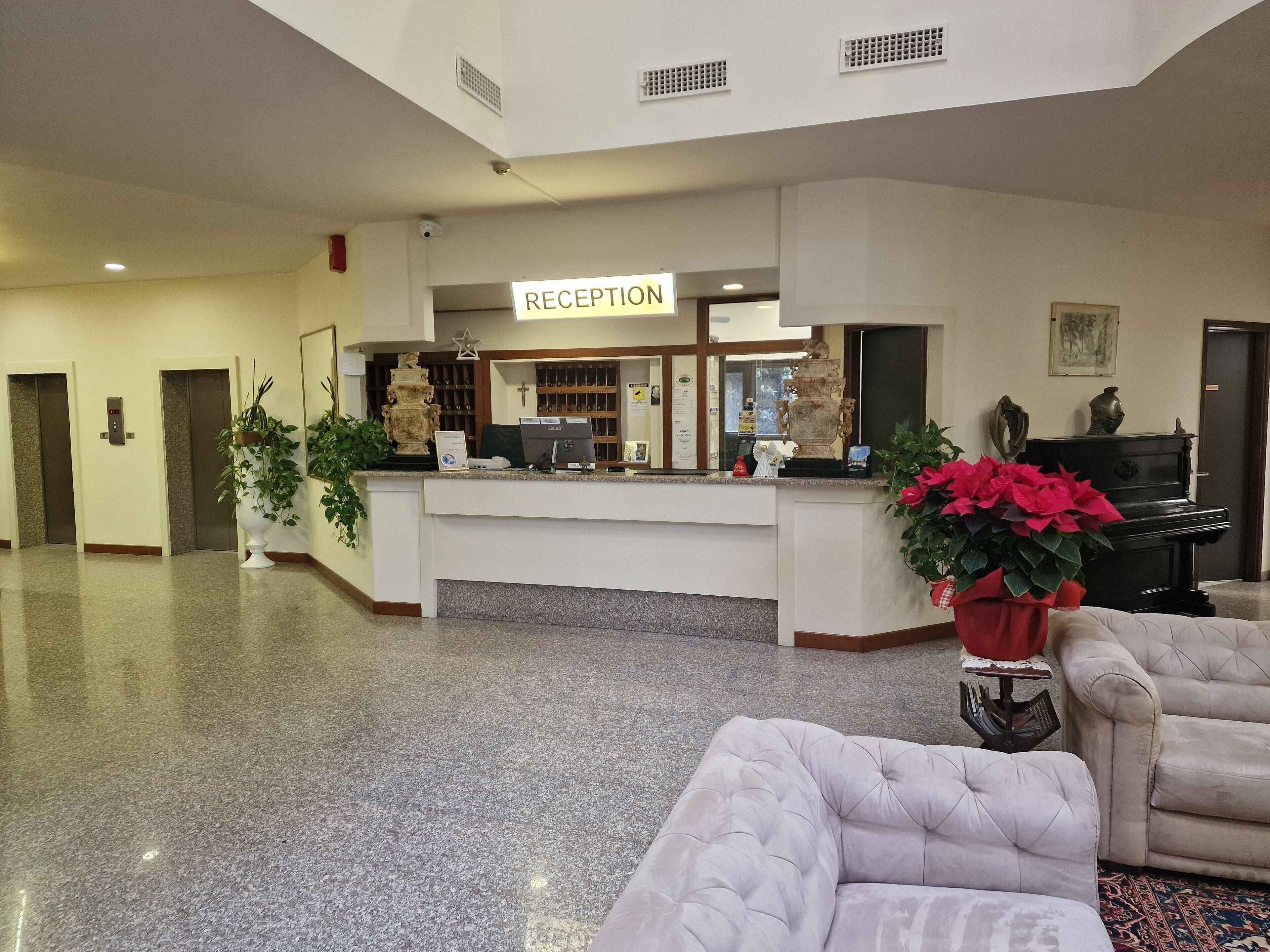 Un área de recepción con mostrador, un piano y un espacio de estar con un sofá capitonado.