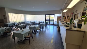 A dining area with tables and chairs, a reception desk, and large windows.