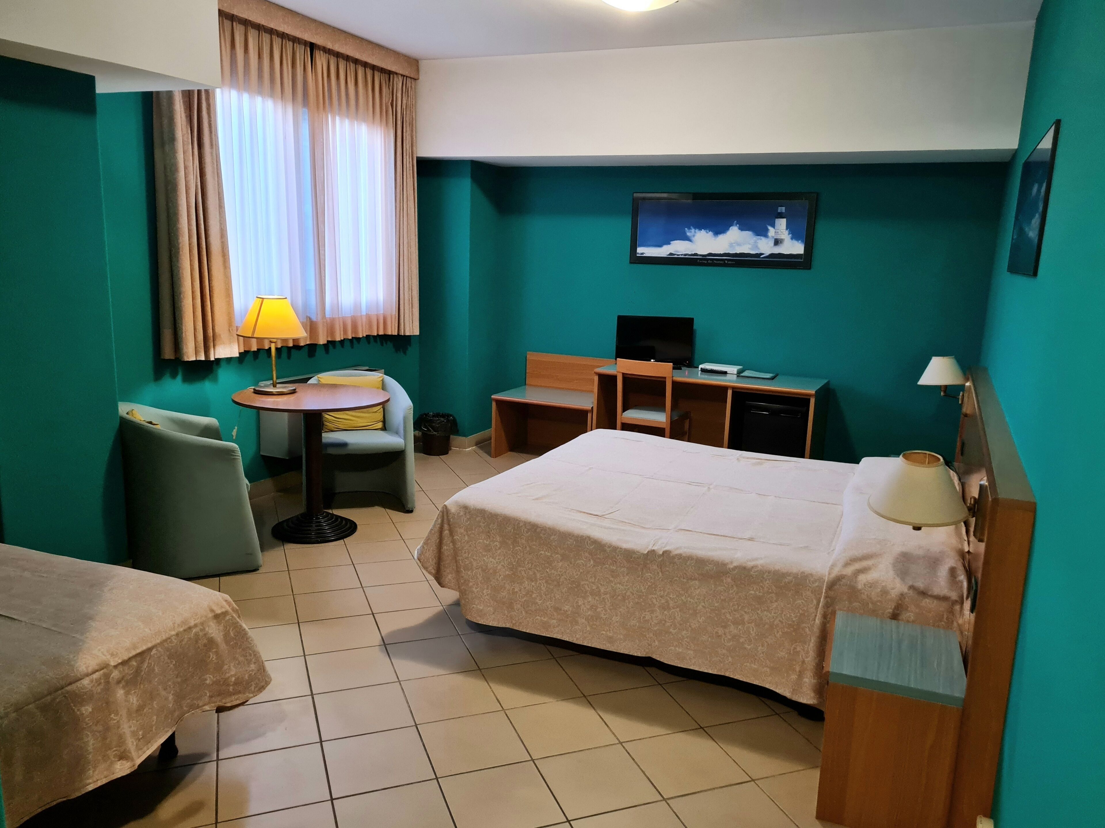 A hotel room with two beds, a desk, a chair, a television, and a window with curtains.