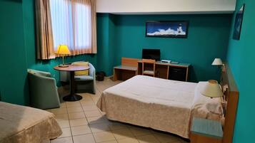 A hotel room with two beds, a desk, a chair, a television, and a window with curtains.