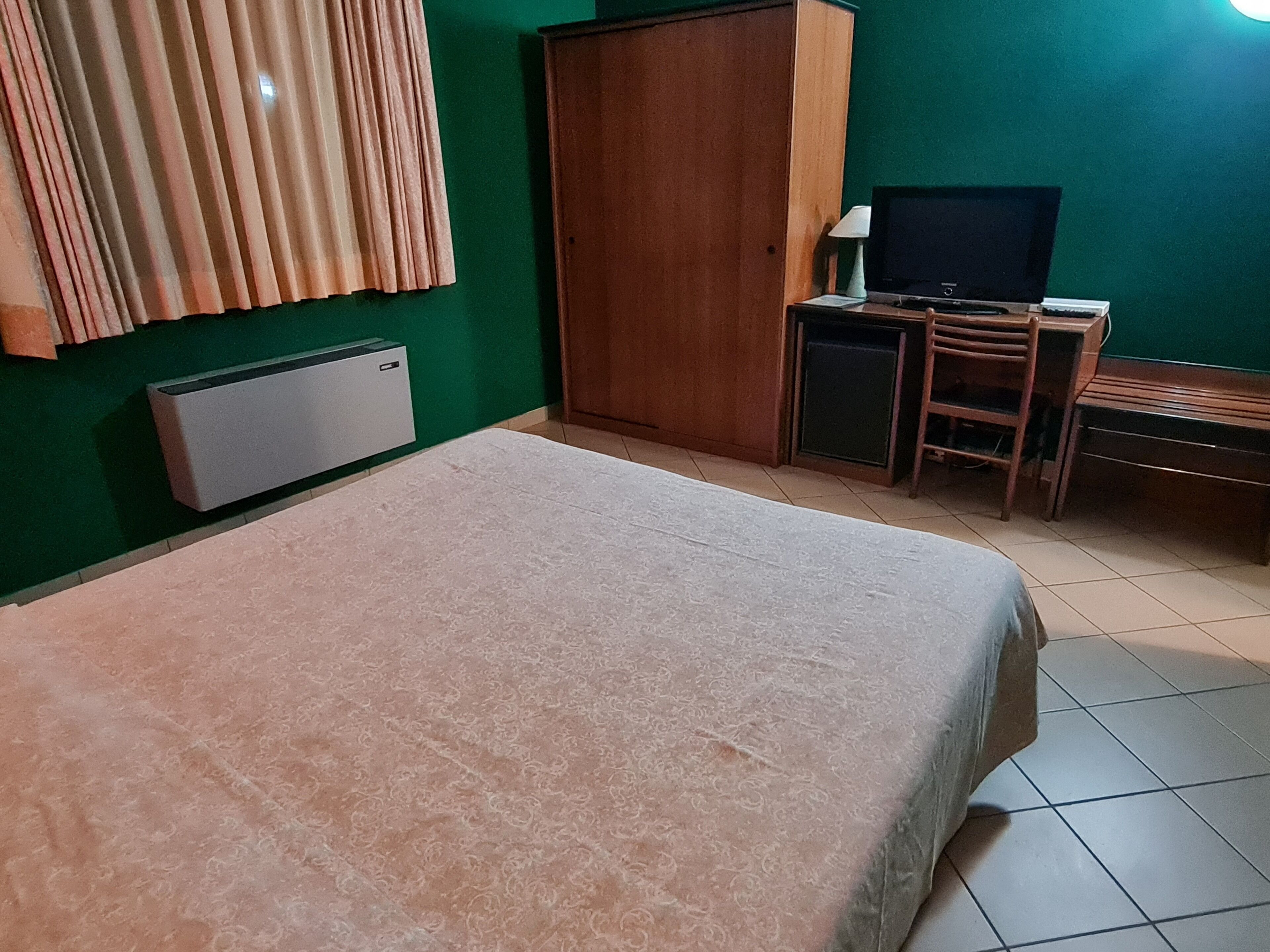 Un dormitorio con cama, escritorio, silla, televisor y armario.