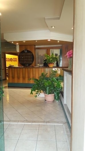 A reception area with a wooden reception desk, potted plants, and a tiled floor.