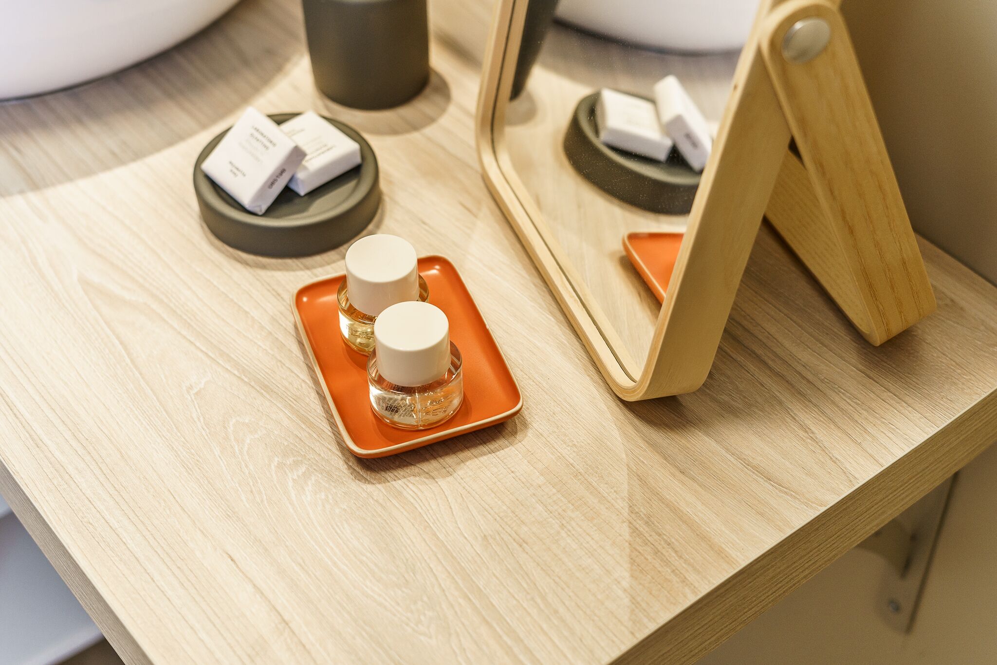 A wooden counter with toiletries on orange trays and a mirror reflecting the setup.