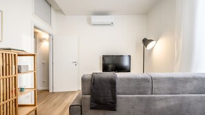 Ein modernes Wohnzimmer mit einem grauen Sofa, einem Holzregal, einem Flachbildfernseher und einer Stehlampe.