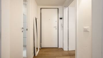 A hallway with a wooden floor, white walls, and a closed door at the end.