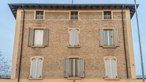 Ein mehrstöckiges Gebäude mit sechs Fenstern, jeweils mit Fensterläden, und einer Ziegel-Fassade.