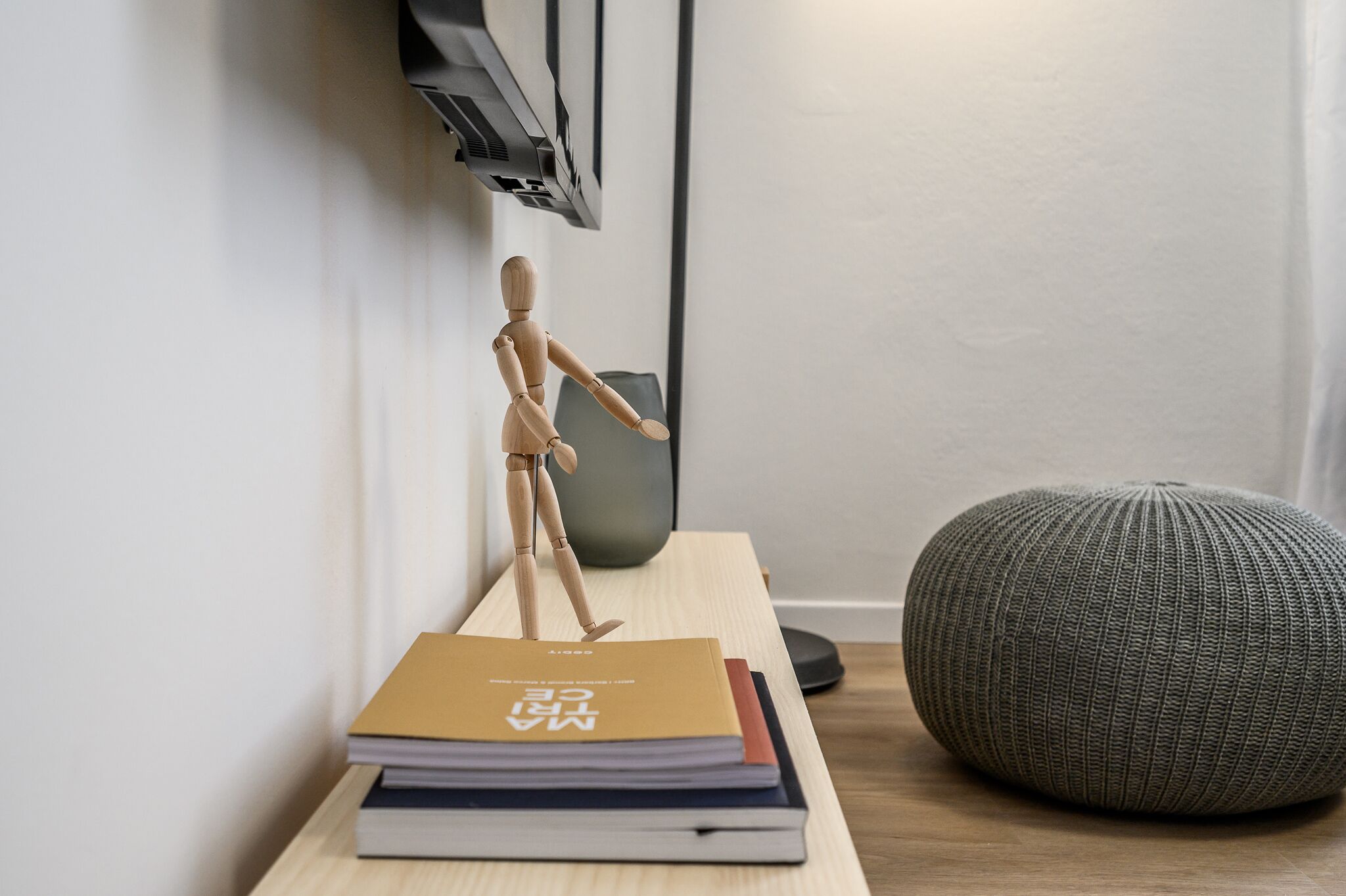 A wooden mannequin on a shelf, a stack of books, and a textured ottoman.