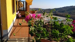 Un bâtiment jaune doté d’un balcon, de plantes en pot et offrant une vue sur des collines.