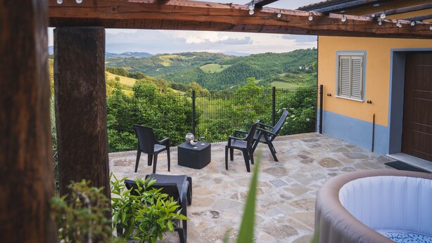 Une terrasse avec des sièges extérieurs, un jacuzzi et une vue panoramique sur des collines verdoyantes.