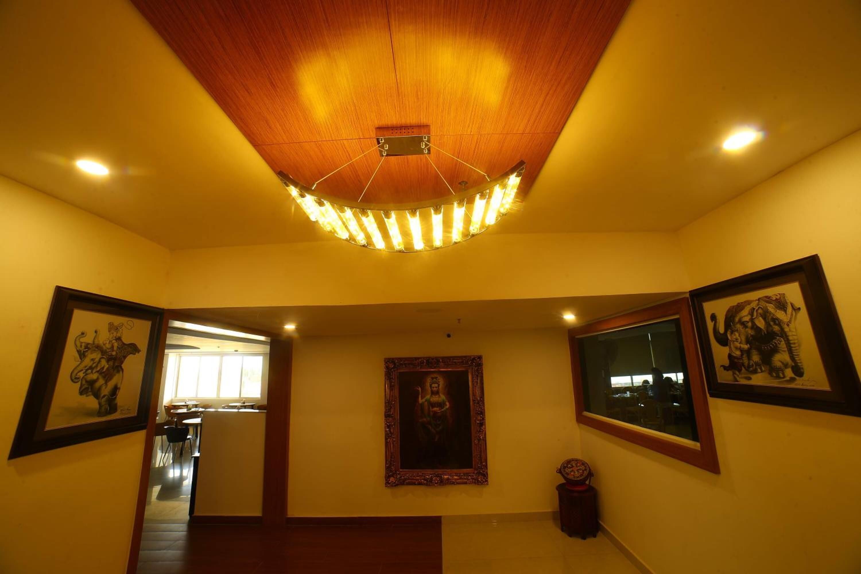 Un couloir aux murs ornés de tableaux encadrés, un plafond en bois avec un luminaire, et une vue sur un espace salle à manger.