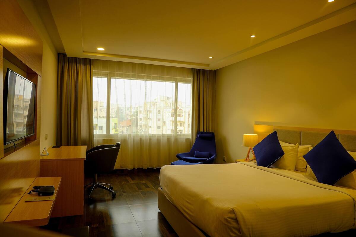 A hotel room with a bed, a desk, a chair, a TV, and a window with curtains.