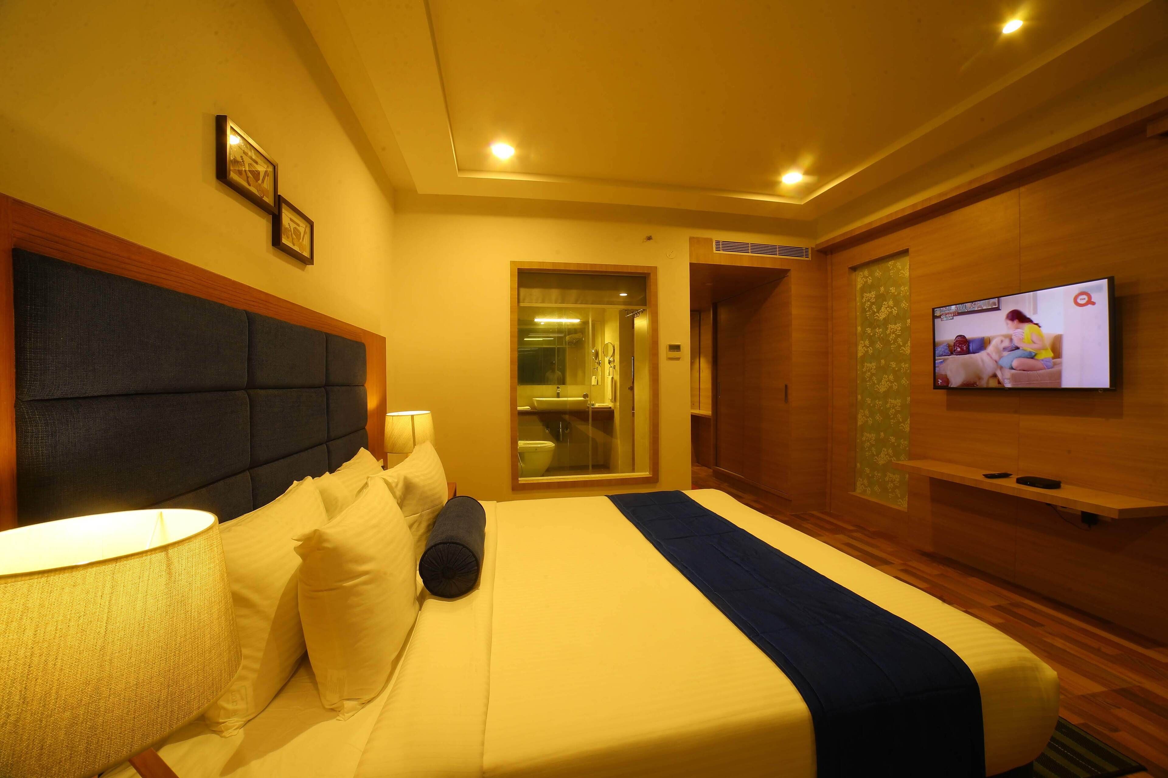 A hotel room with a bed, a TV, a lamp, and a wooden headboard.