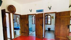 A room with a red patterned floor, wooden doors, and a view into another room with a bed and a window.