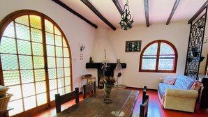 A dining area with a wooden table and chairs, a fireplace, and large arched windows.