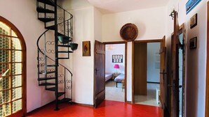 A hallway with a red patterned floor, a black spiral staircase, and a door leading to a bedroom.