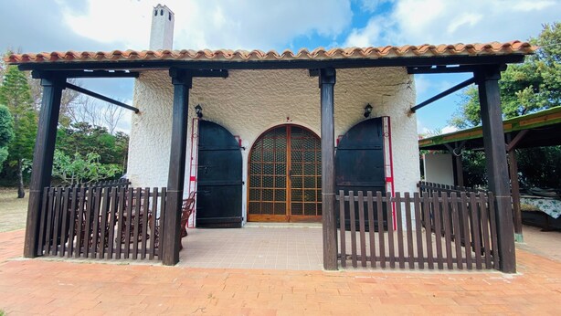 A covered outdoor area with a tiled roof, a wooden fence, and a large arched door.
