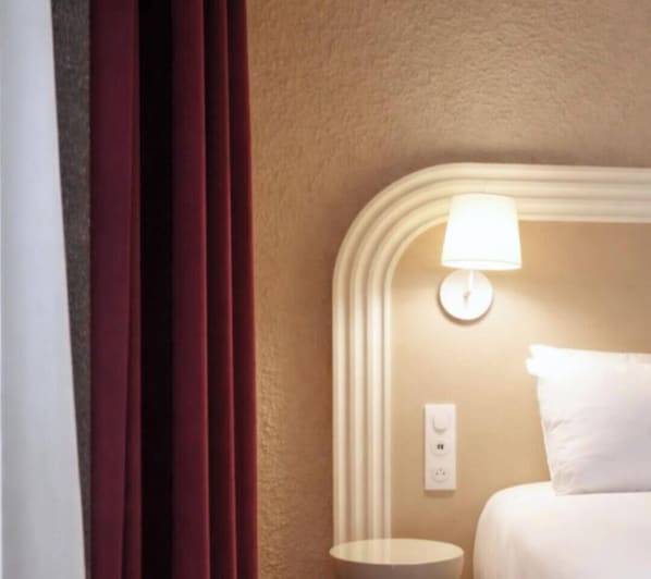 A hotel room with a bed, a bedside lamp, a nightstand, and a window with curtains. - Résidence les Dômes by Vy Resort Thermal & Spa (Vichy)