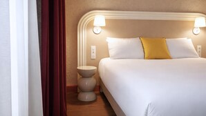 Una cama bien hecha con almohadas blancas y amarillas, una mesita de noche redonda y dos lámparas de pared.
