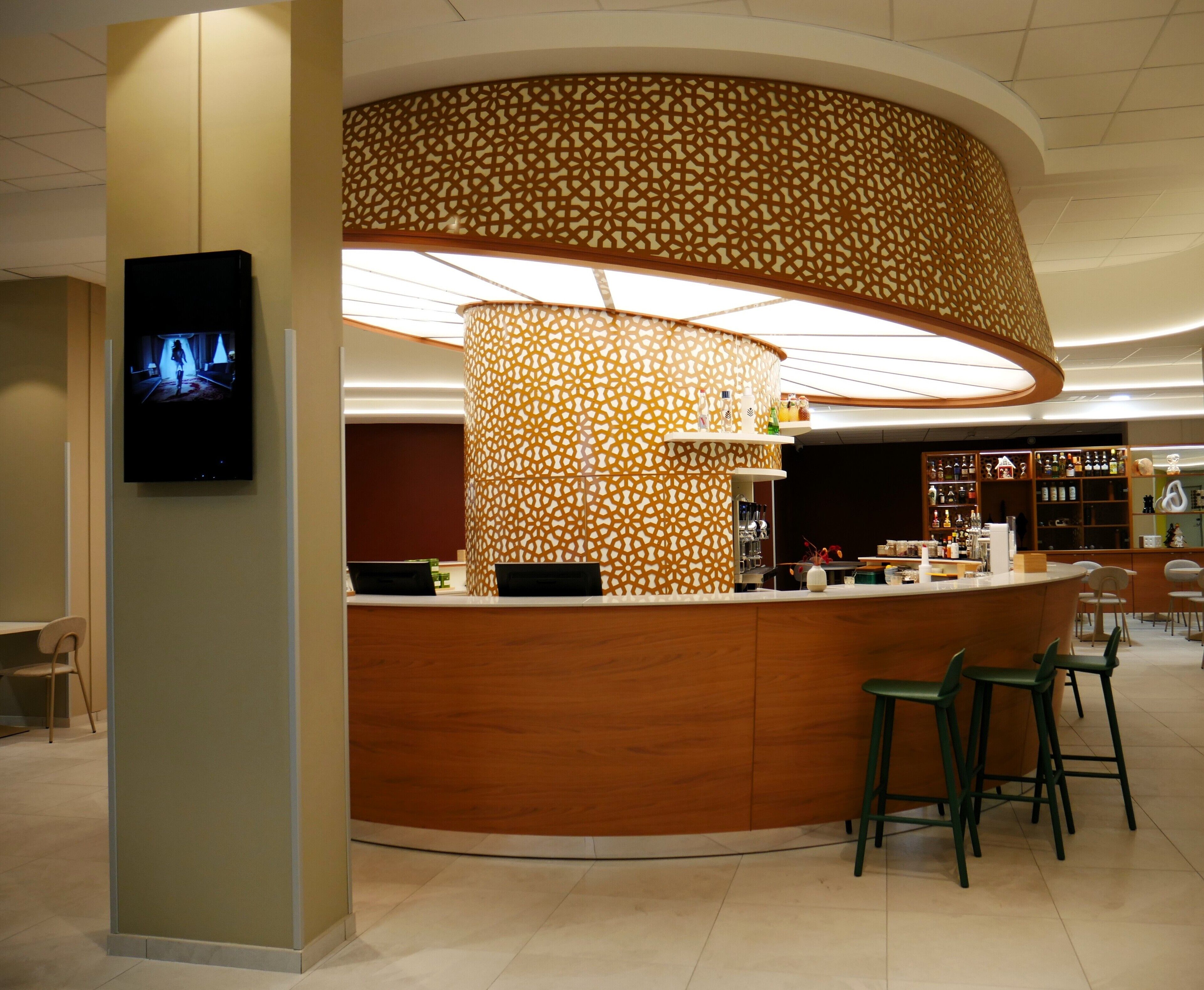 Un espace bar moderne avec un comptoir incurvé, des tabourets de bar et un mur décoratif orné de motifs.