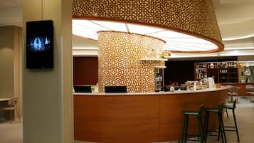 Un espace bar moderne avec un comptoir incurvé, des tabourets de bar et un mur décoratif orné de motifs.