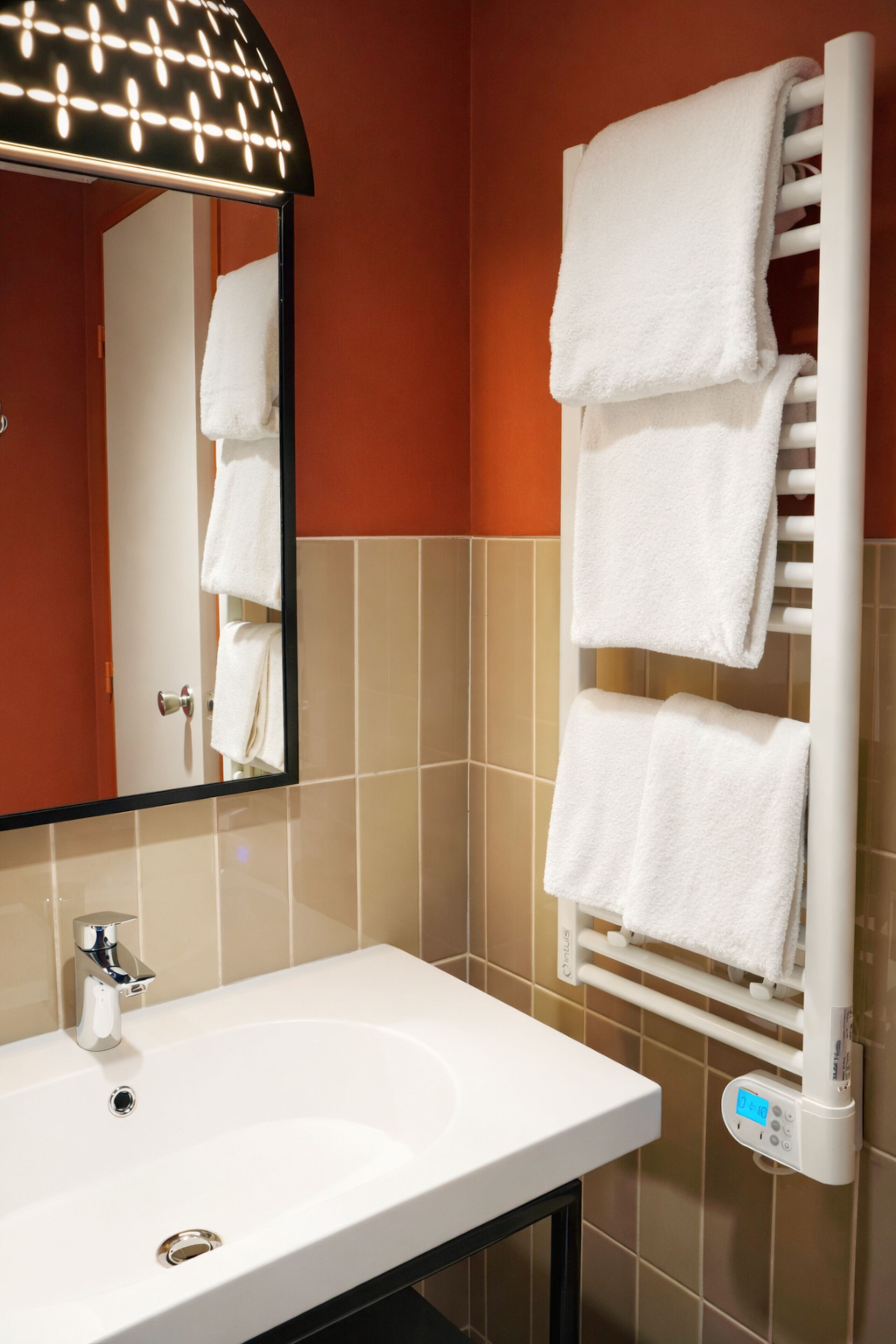 A bathroom with a white sink, a towel rack with multiple towels, a mirror with lights, and a digital display.