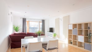 A modern living room with a white dining table, two white chairs, a red sofa, and a bookshelf. - Serenity Apartment Whitechapel (London)