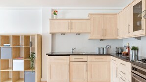 A kitchen with light wooden cabinets, a black countertop, and a stainless steel sink. - Serenity Apartment Whitechapel (London)