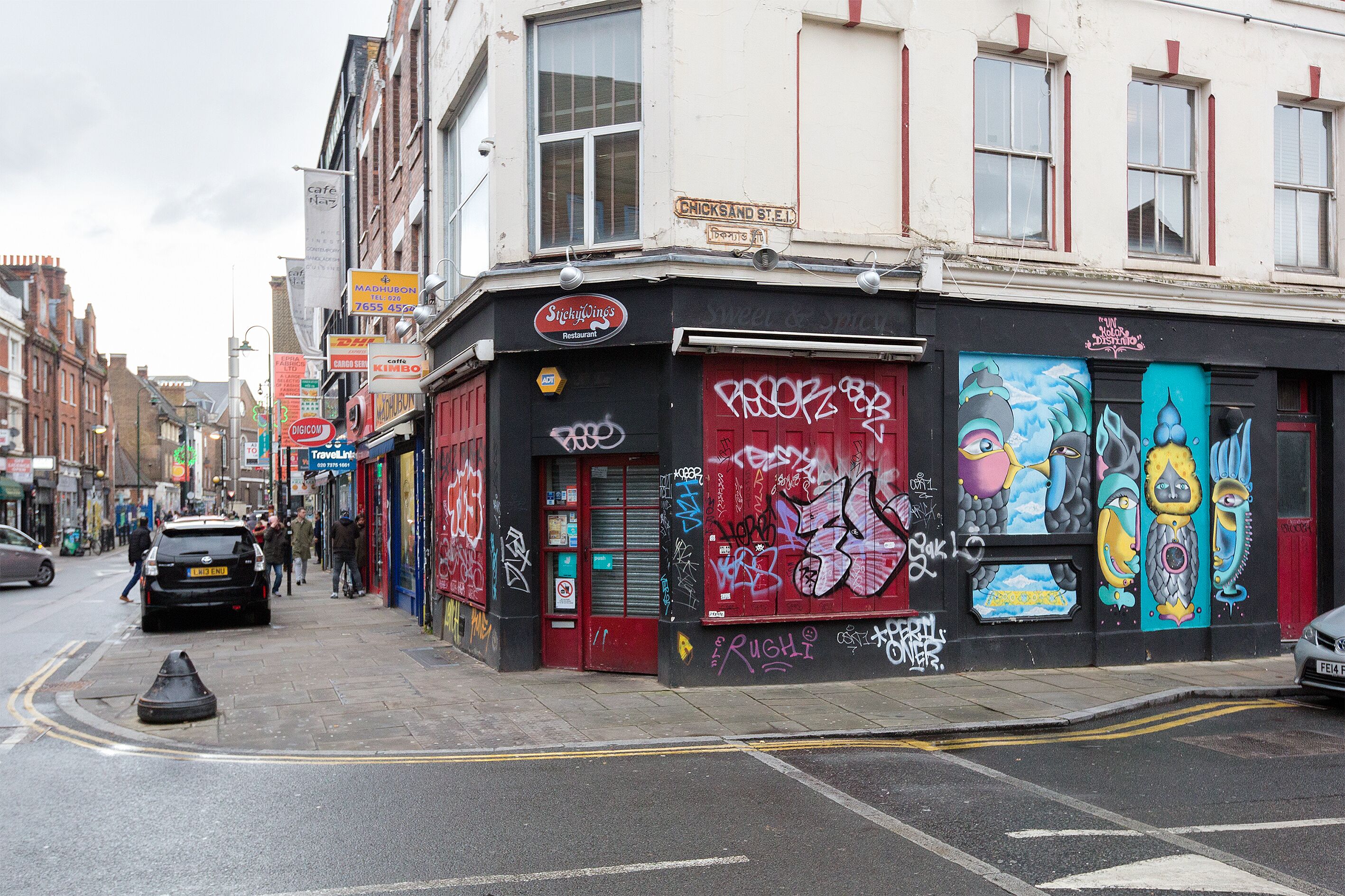 A street view with a building featuring a closed shop with graffiti and a red door.