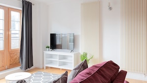 A modern living room with a flat-screen TV on a white stand, a red sofa, and a white side table with a plant. - Serenity Apartment Whitechapel (London)