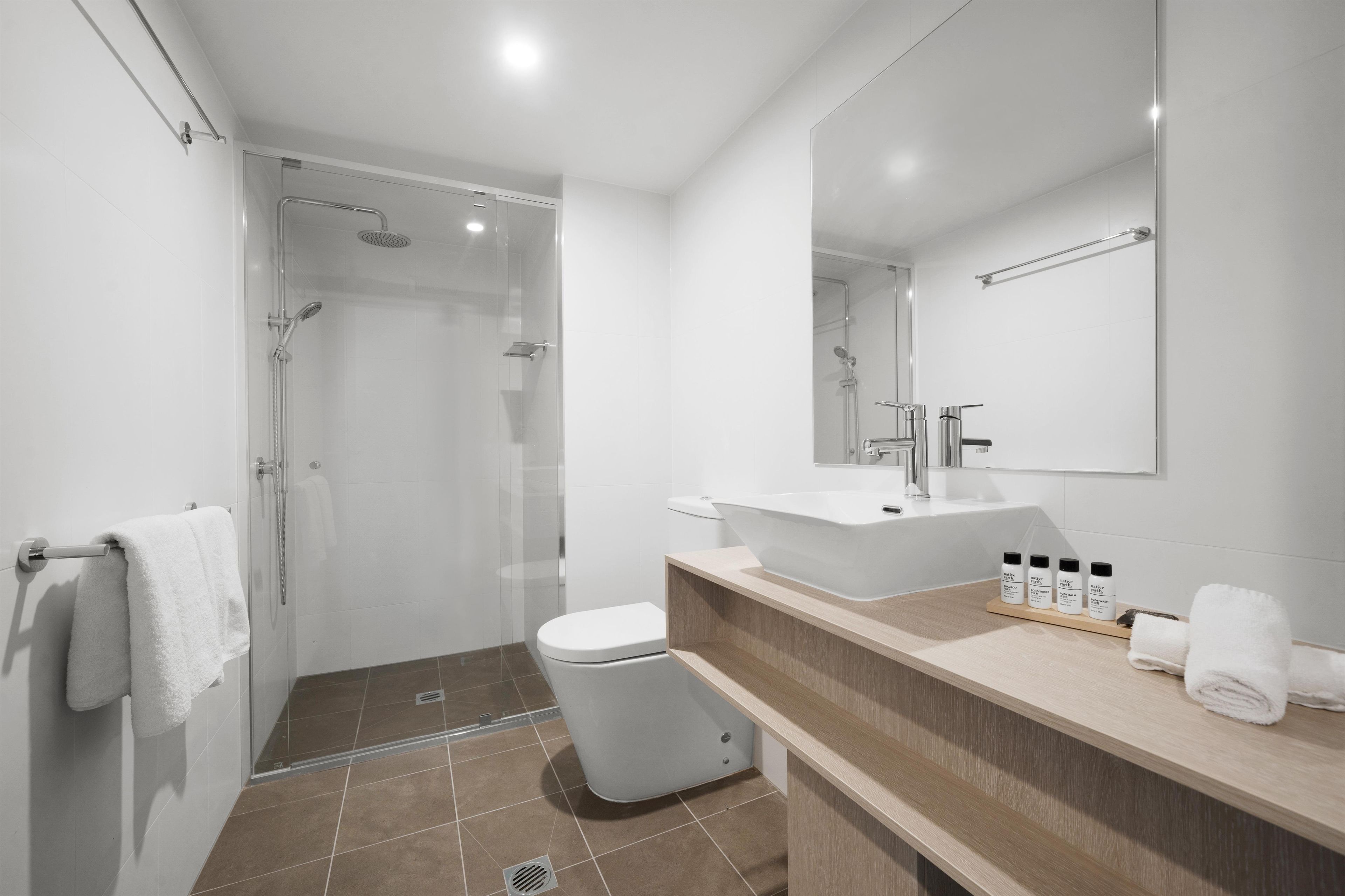 A modern bathroom with a glass-enclosed shower, a white toilet, and a vanity with a large mirror and sink.