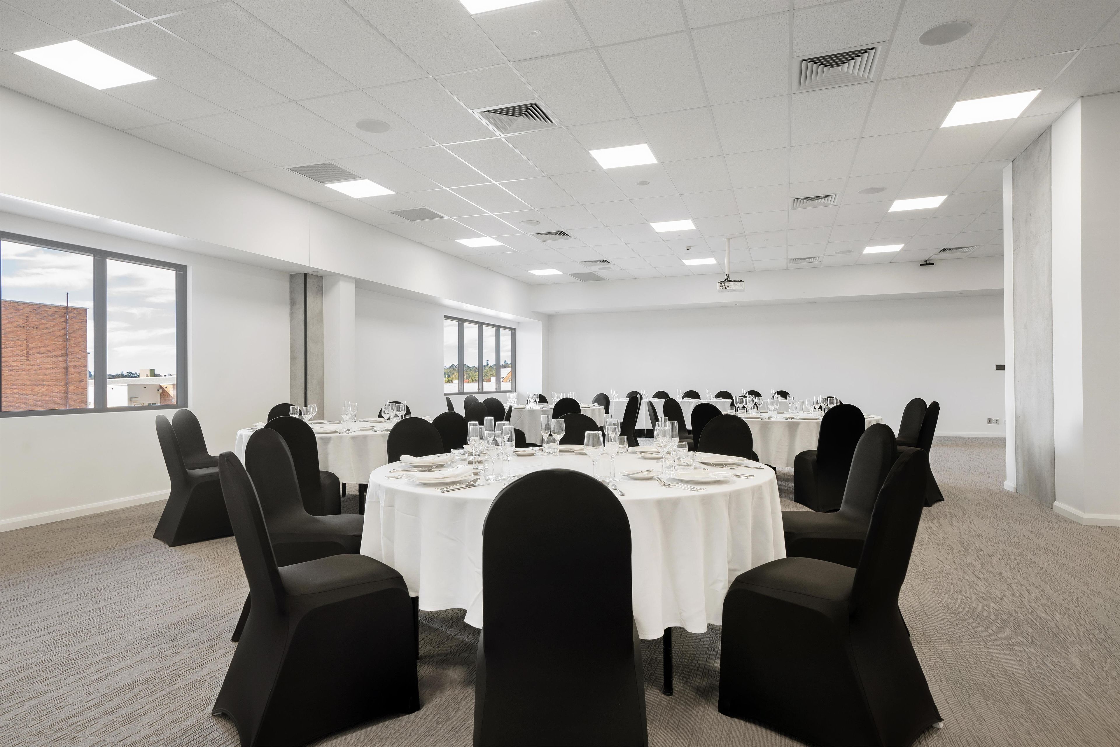 Een vergaderzaal met ronde tafels, zwarte stoelen en witte tafelkleden.