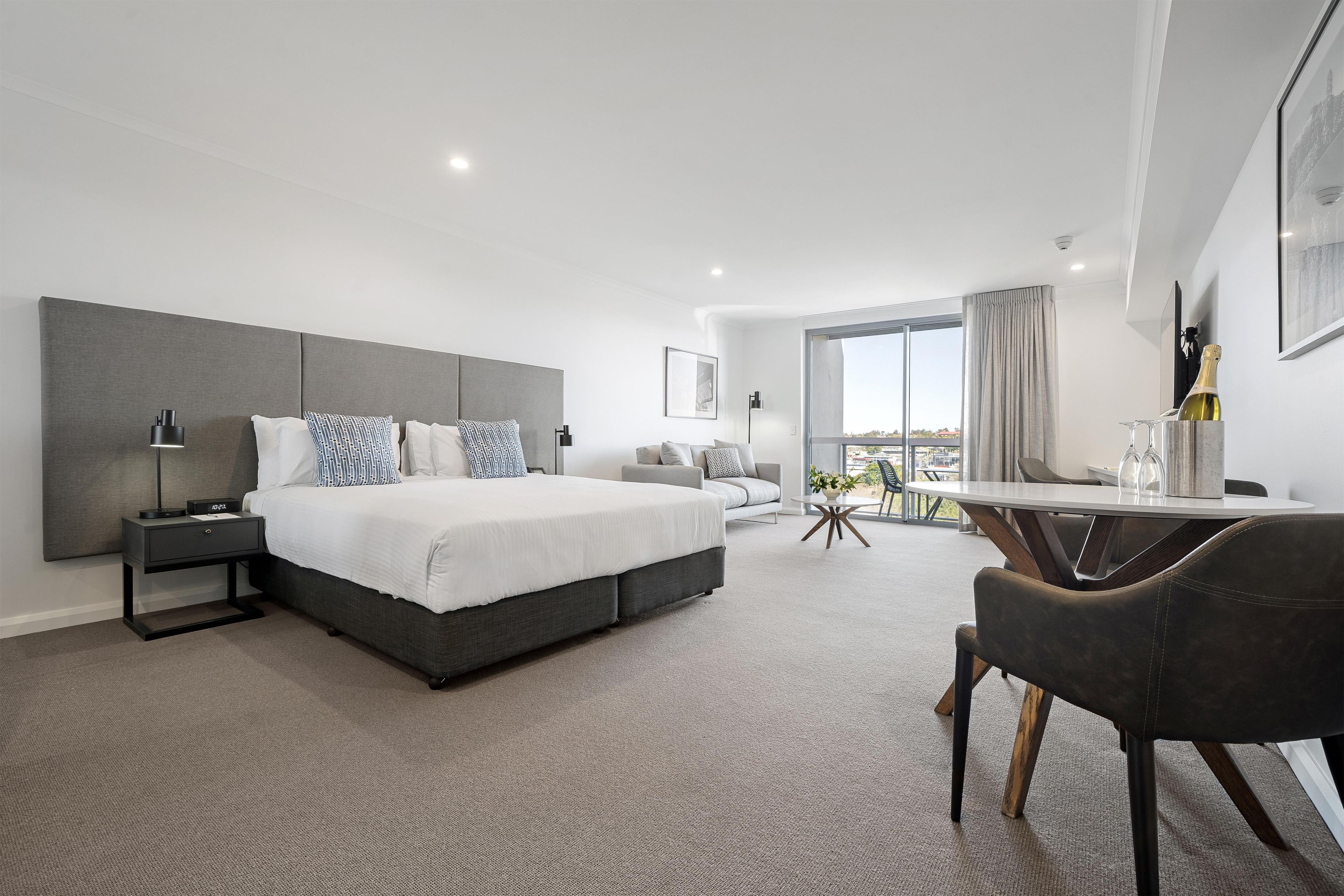 A modern hotel room with a large bed, a desk, and a view of the city.