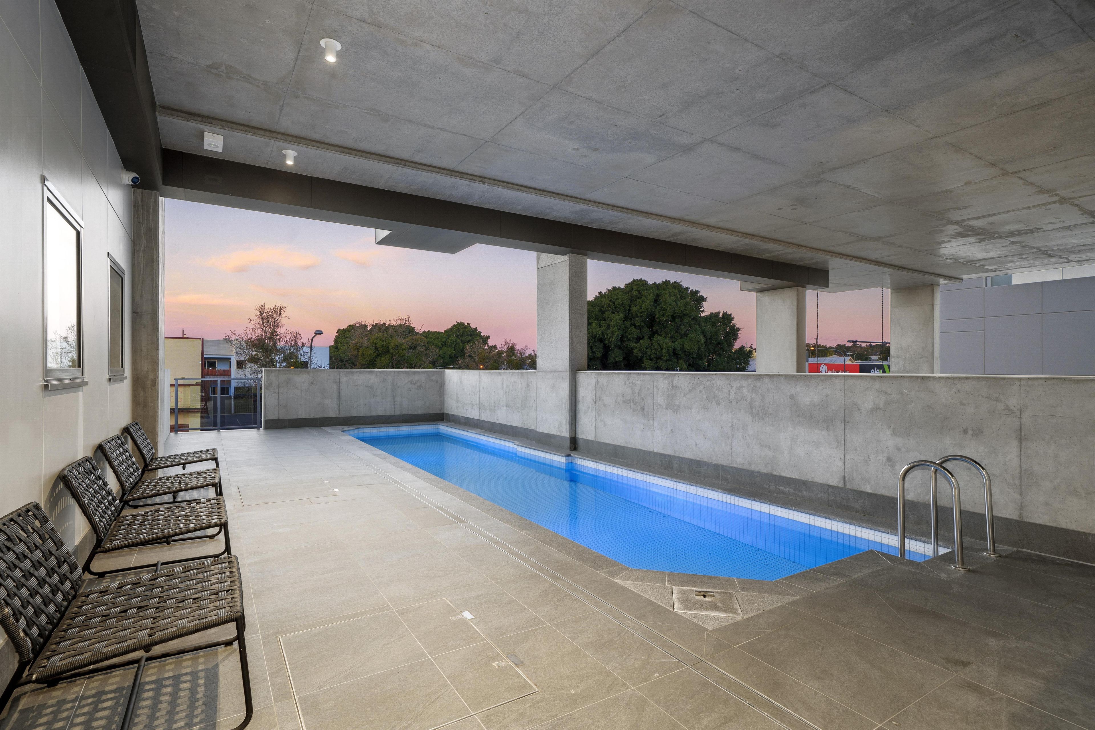 An indoor swimming pool with a view of the sunset, concrete walls, and seating area.