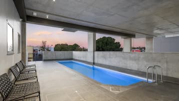 An indoor swimming pool with a view of the sunset, concrete walls, and seating area.