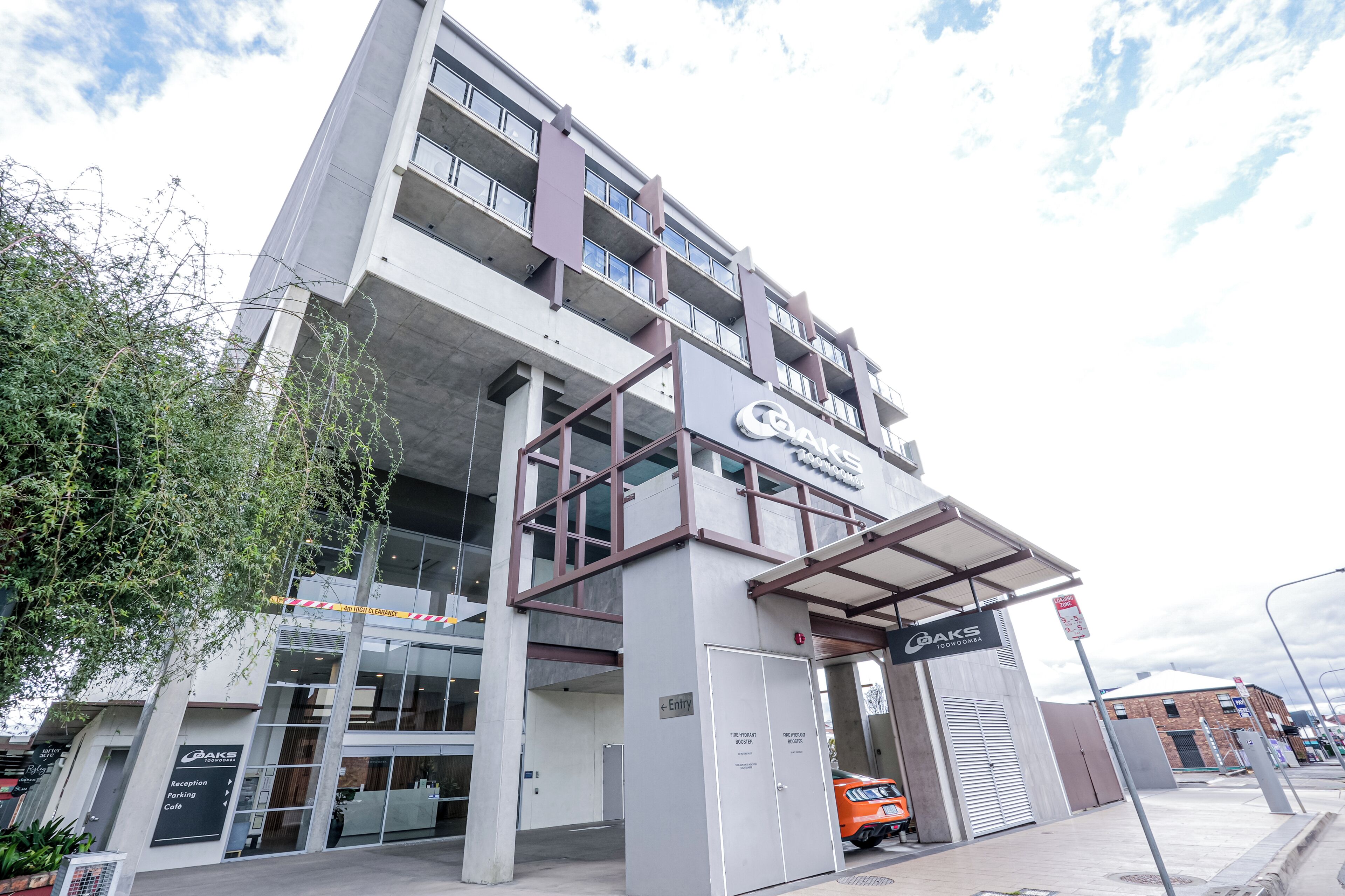 A multi-story building with a prominent sign for 'QAKS TOOWOOMBA' and a fire hydrant booster sign.