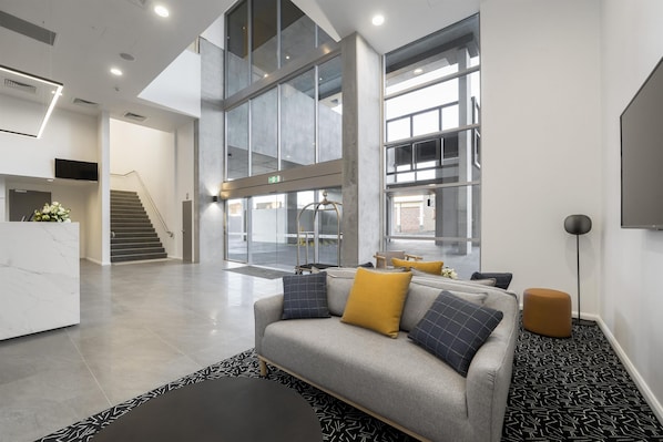 A spacious lobby with a grey sofa, a reception desk, and large windows.