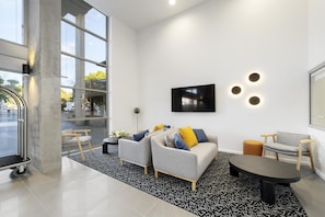 A modern living room with a sofa, chairs, a coffee table, and a TV mounted on the wall. - Oaks Toowoomba Hotel (Toowoomba)