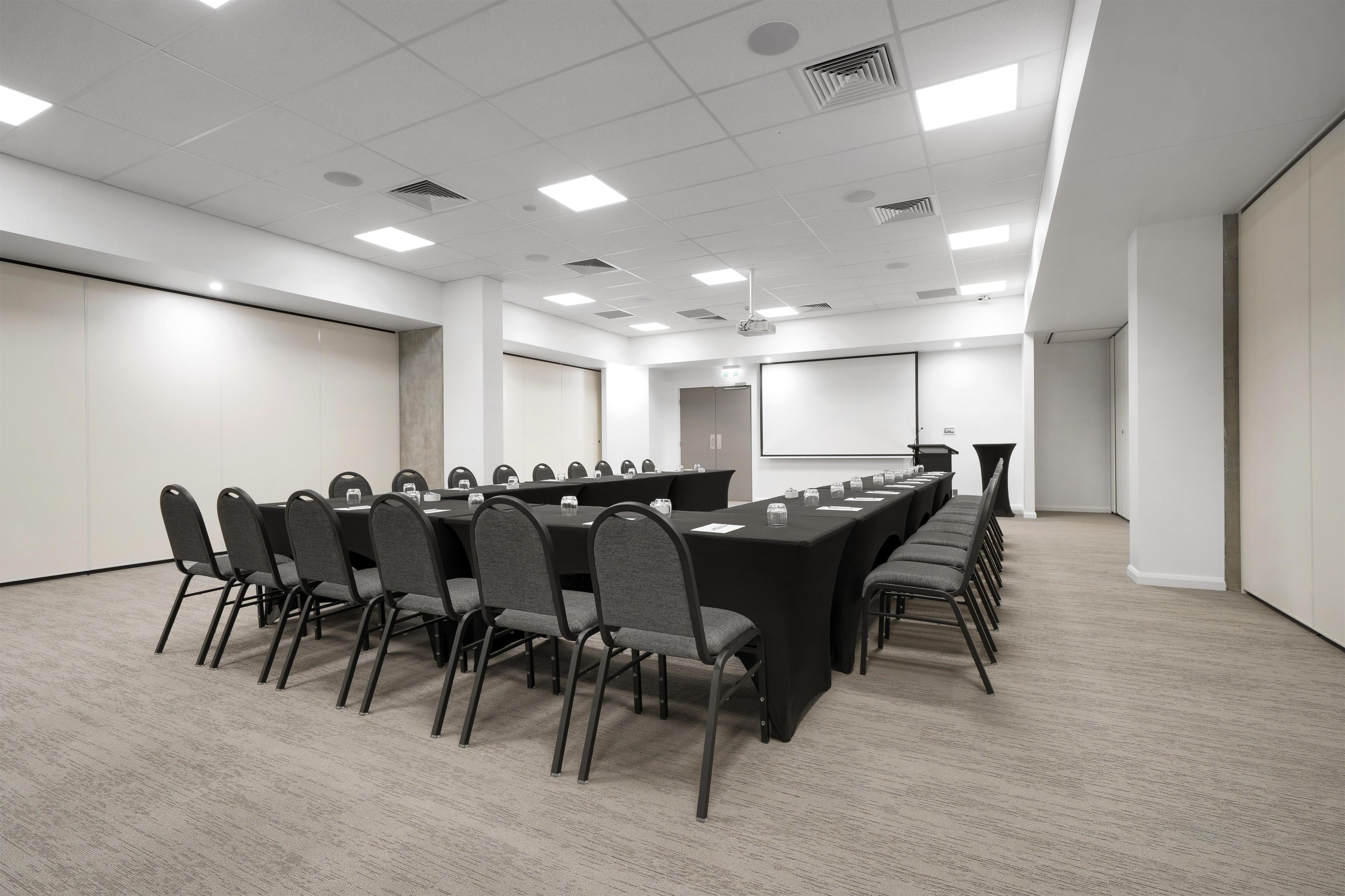 A conference room with a long table, chairs, a projector screen, and a whiteboard.