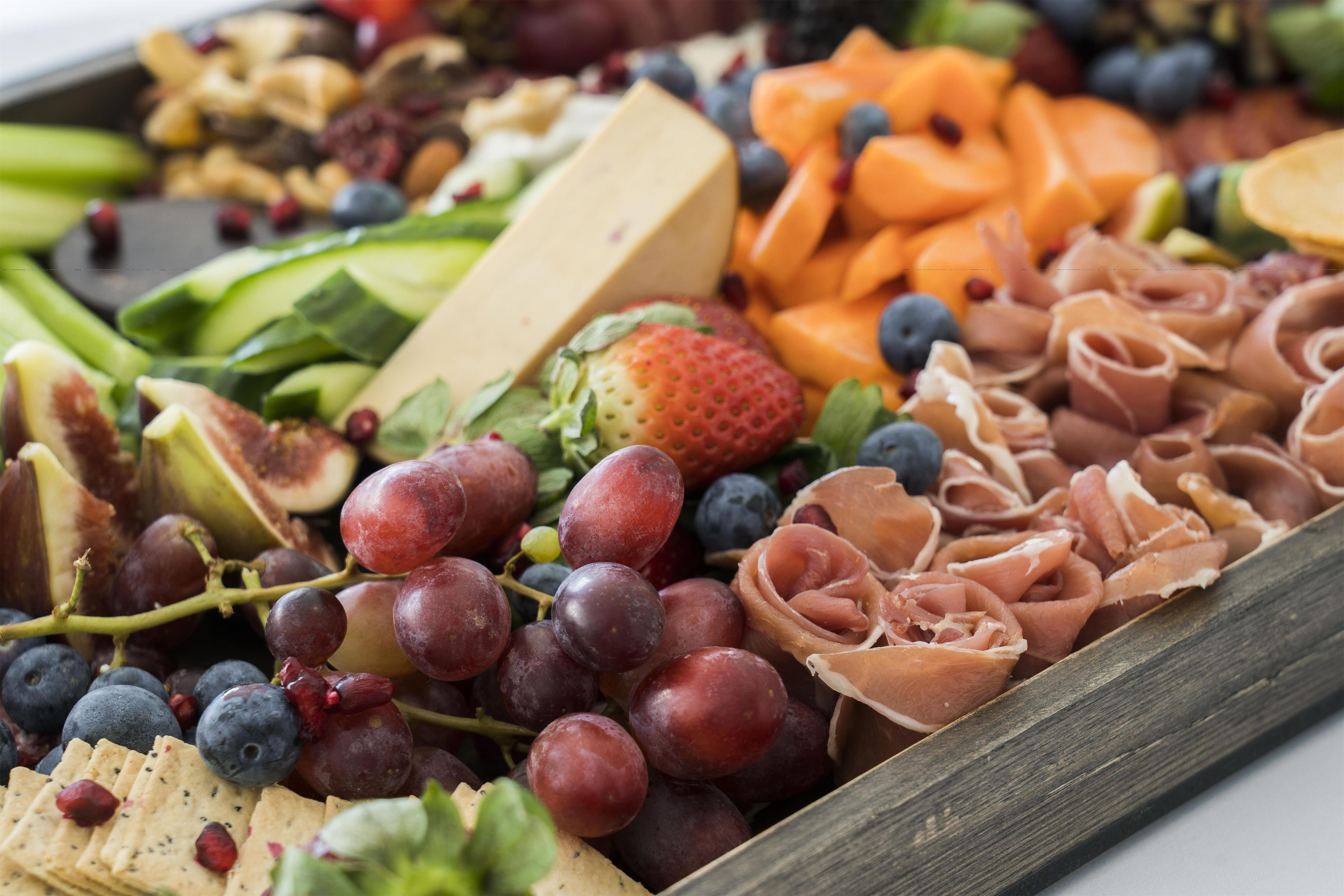 Uma tábua de frios com diversos queijos, frutas e carnes.