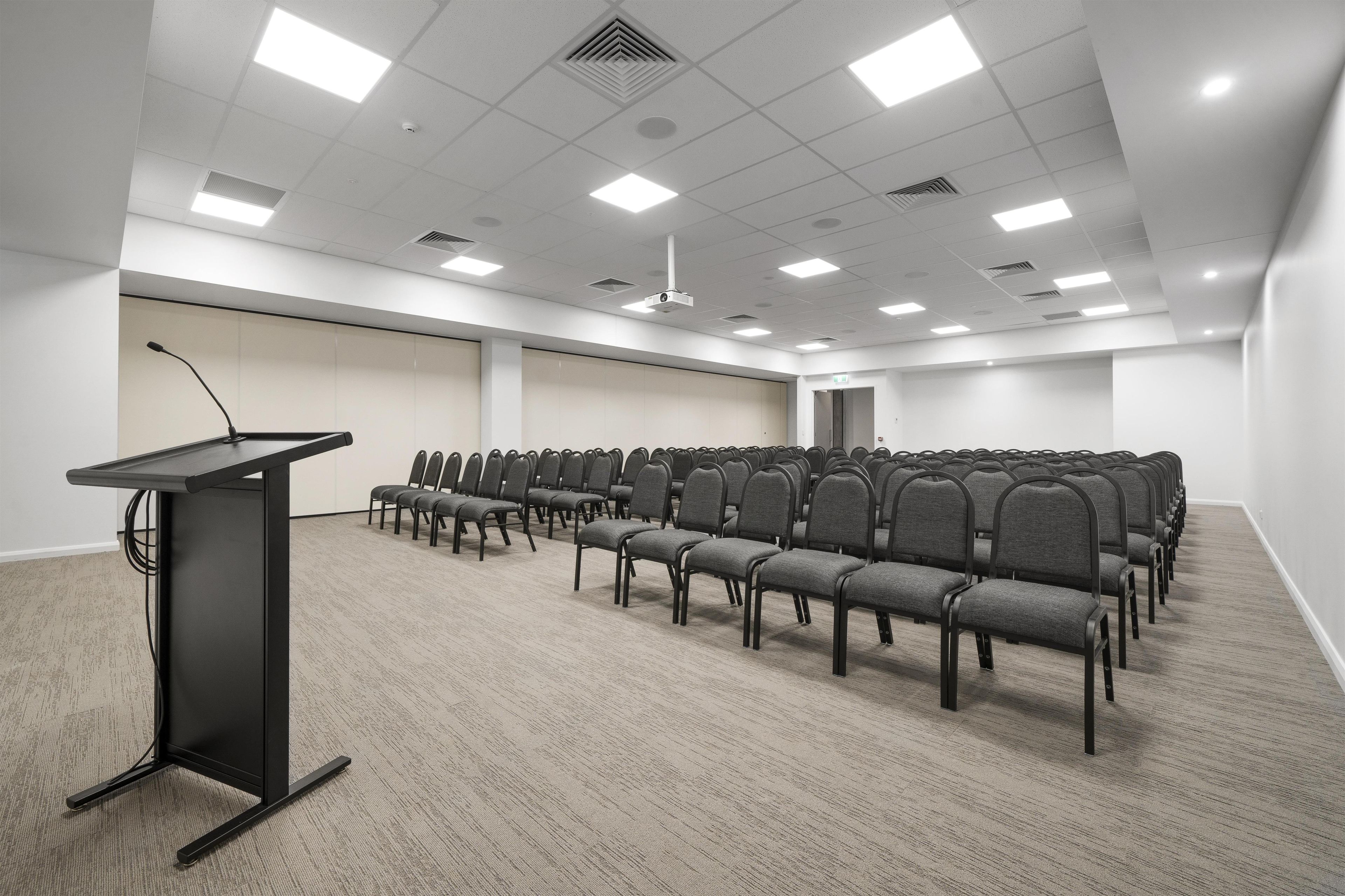 A conference room with rows of chairs, a podium, and ceiling lights.