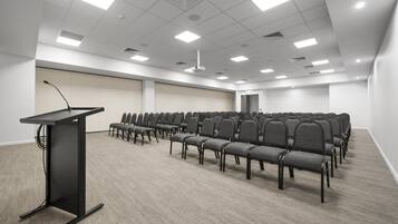 A conference room with rows of chairs, a podium, and ceiling lights.