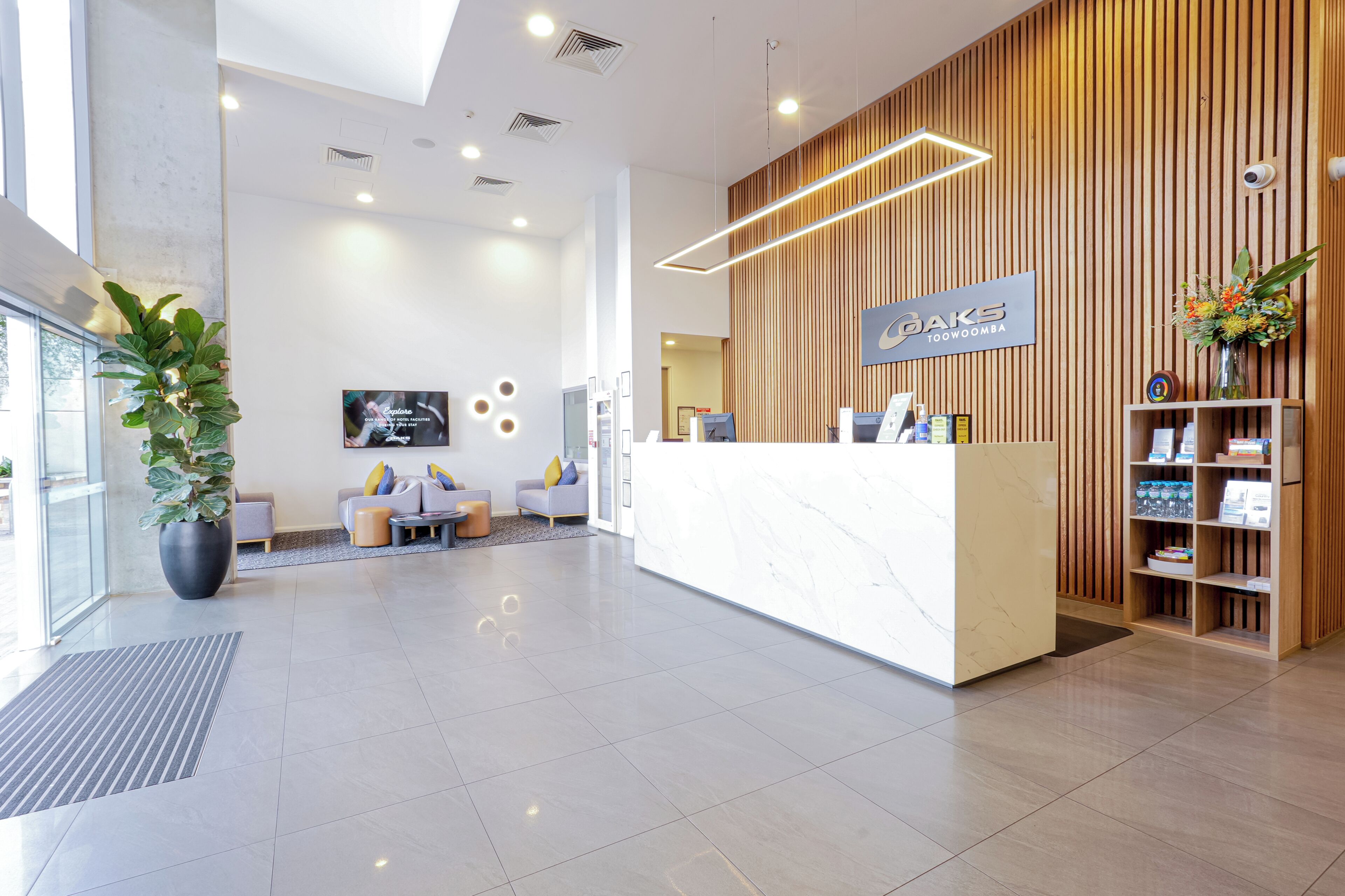 A hotel reception area with a modern design, including a reception desk, seating area, and a wooden panel wall.