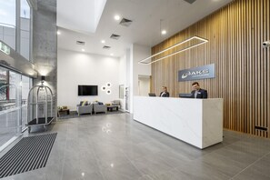 A modern reception area with a wooden panel wall, a marble reception desk, and a flat-screen TV mounted on the wall. - Oaks Toowoomba Hotel (Toowoomba)