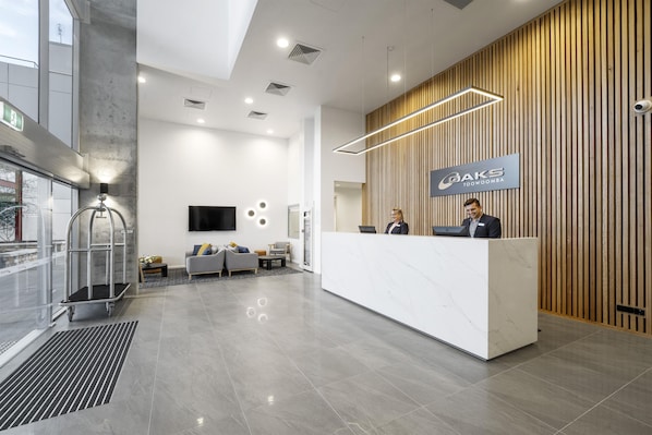 Una moderna zona de recepción con un panel de pared de madera, un mostrador de recepción de mármol y un televisor de pantalla plana montado en la pared.