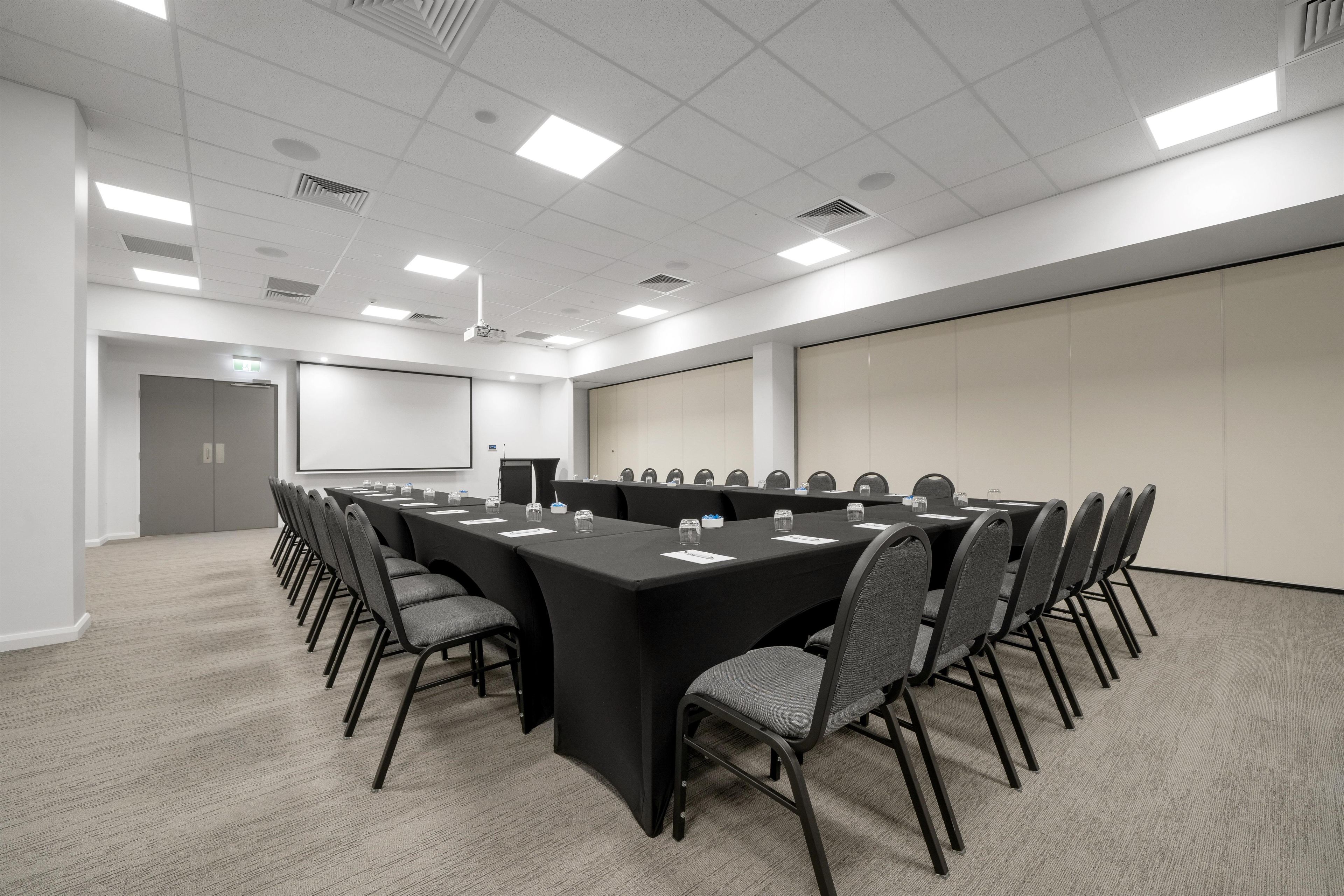 A conference room with a long table, chairs, a projector screen, and a whiteboard.