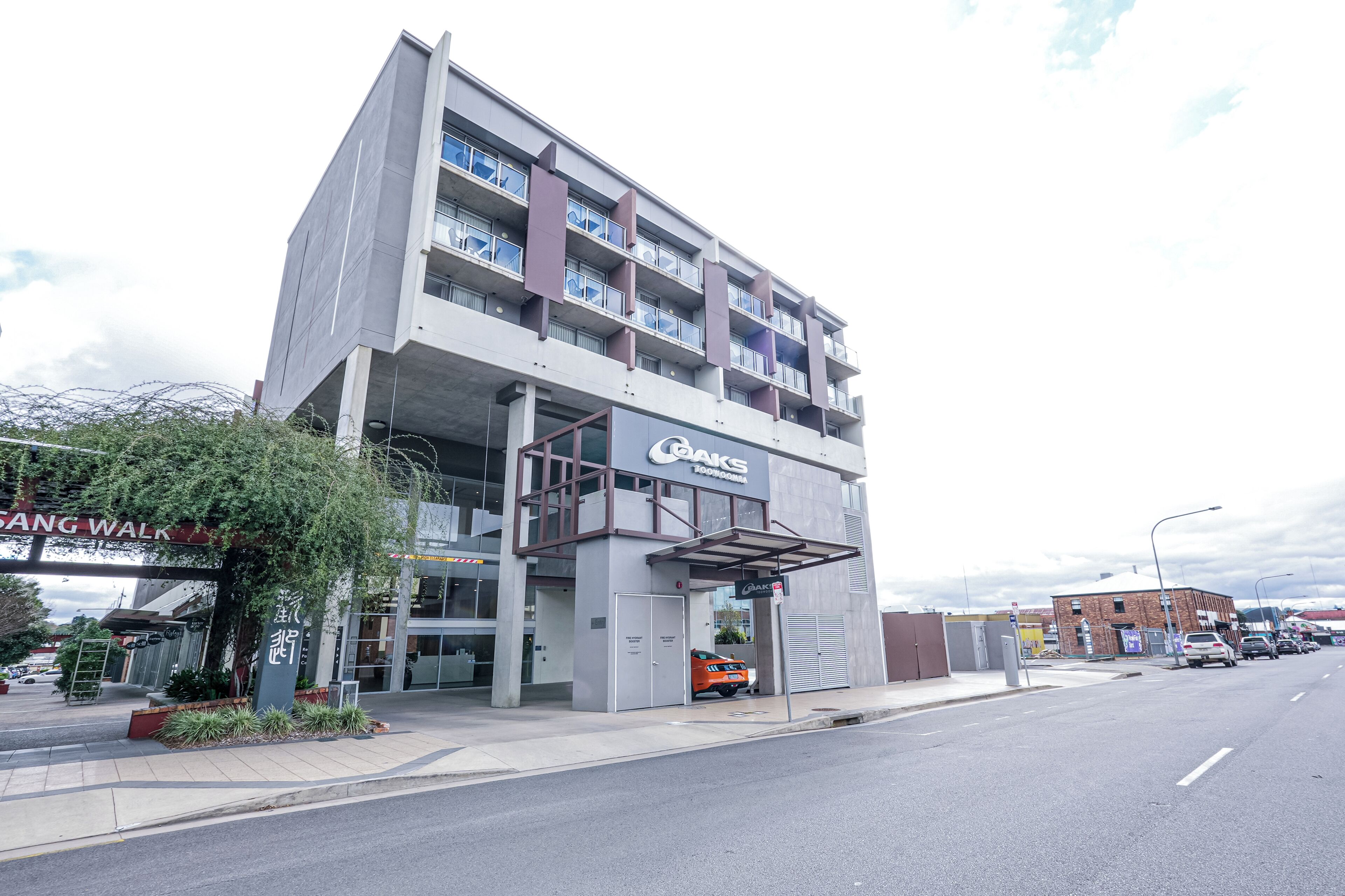 A multi-story building with a prominent sign for 'OAKS' on the ground floor, a covered entrance, and a parking area in front.