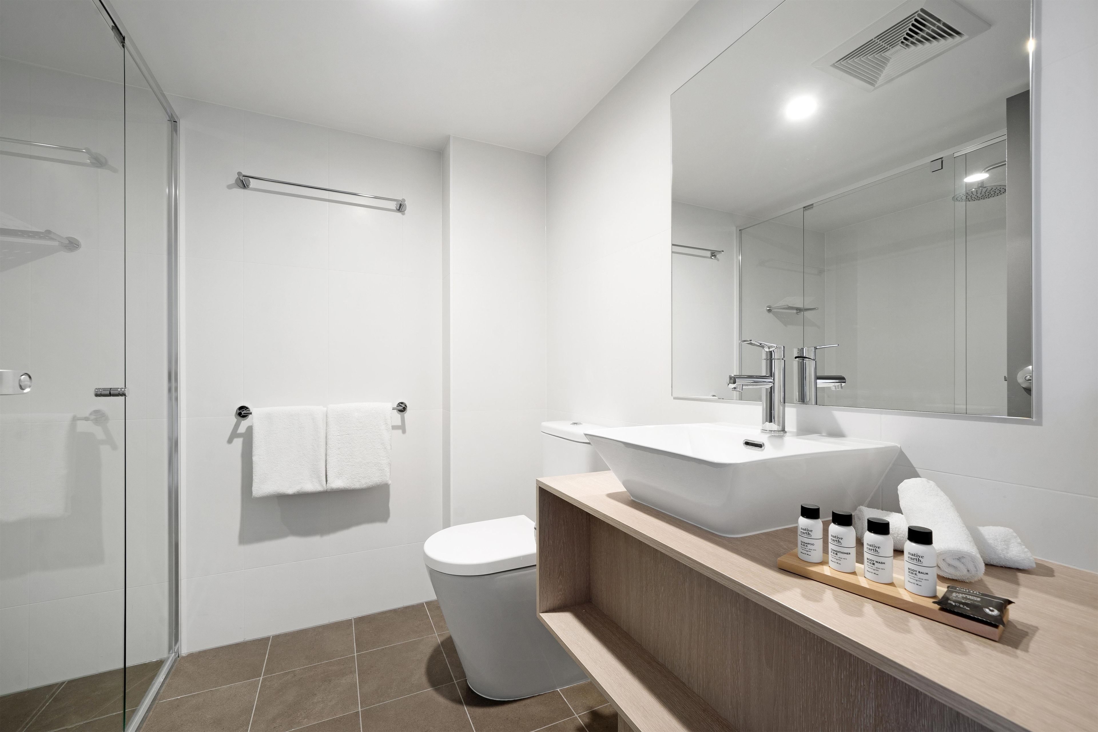 A modern bathroom with a glass shower enclosure, a white toilet, a large sink with a mirror above, and a vanity with toiletries.