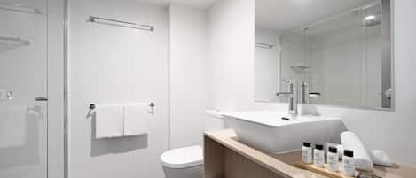 A modern bathroom with a glass shower enclosure, a white toilet, a large sink with a mirror above, and a vanity with toiletries.