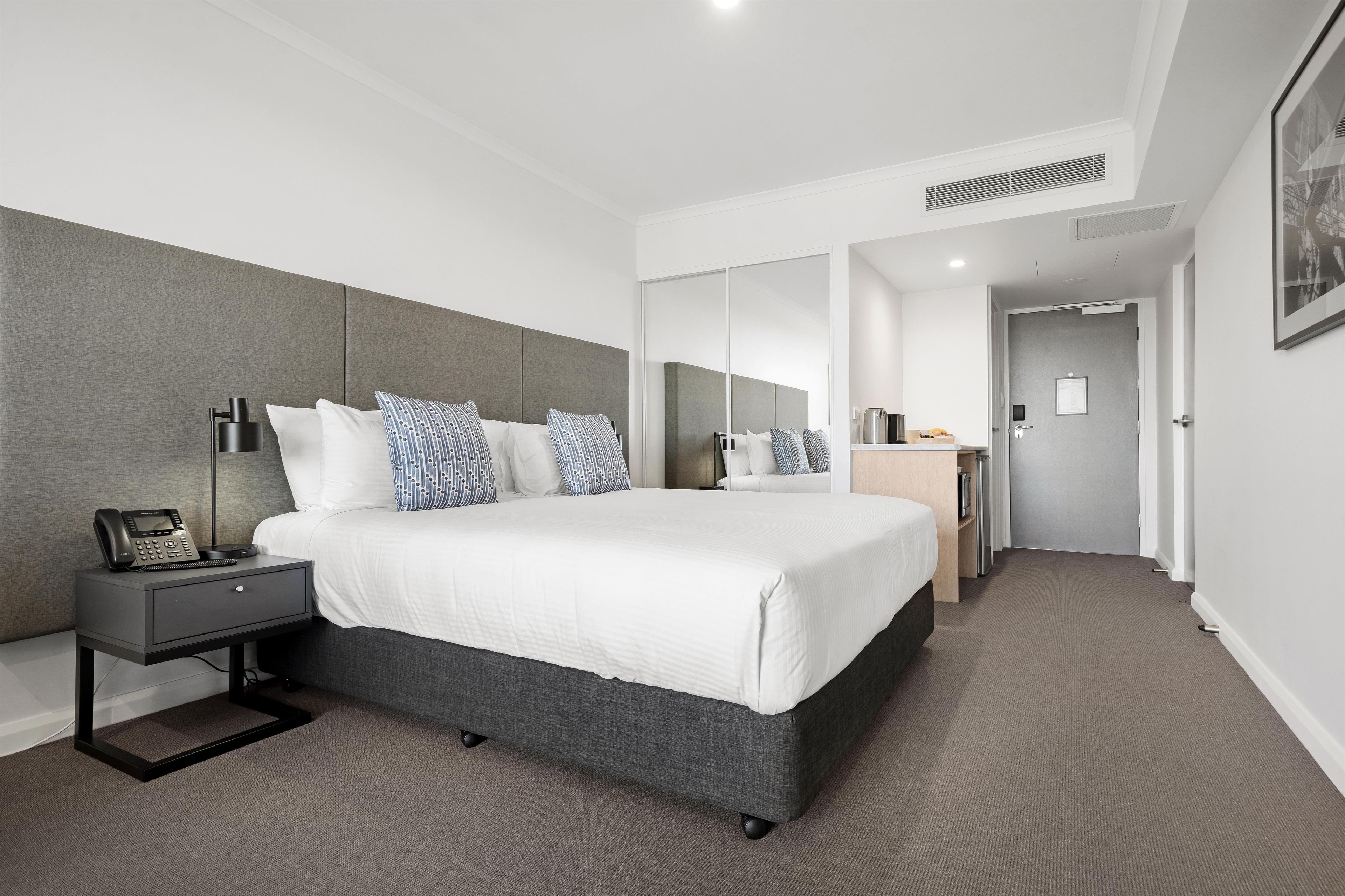 A modern hotel room with a large bed, bedside table, and a desk with a telephone.